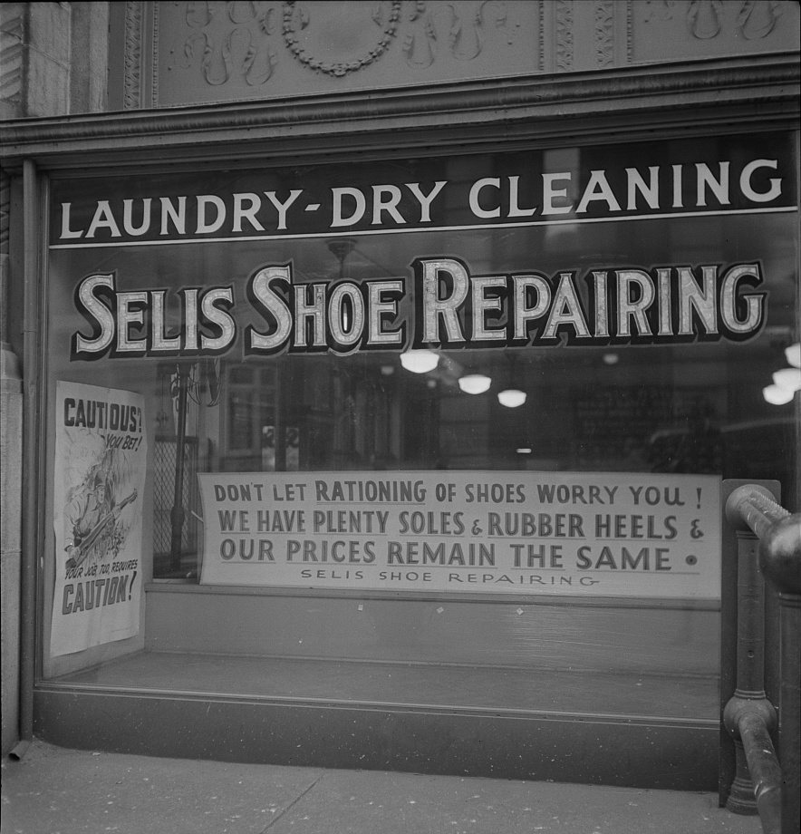 Black-and-white photograph of a shop window lettered “Selis Shoe Repairing”, with a sign reading “Don’t let rationing of shoes worry you! We have plenty soles and rubber heels and our prices remain the same”